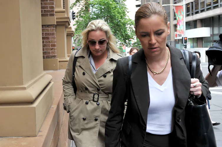A blonde woman in a trench coat walks alongside a brunette woman in a suit