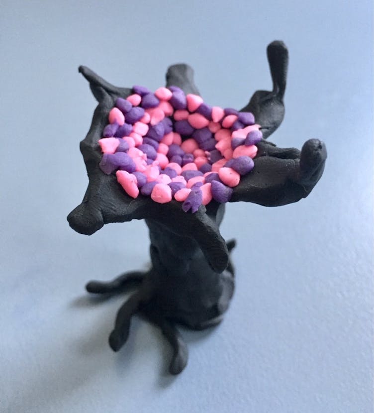 A black tree sculpture made of clay, with pink and purple dots in the centre.
