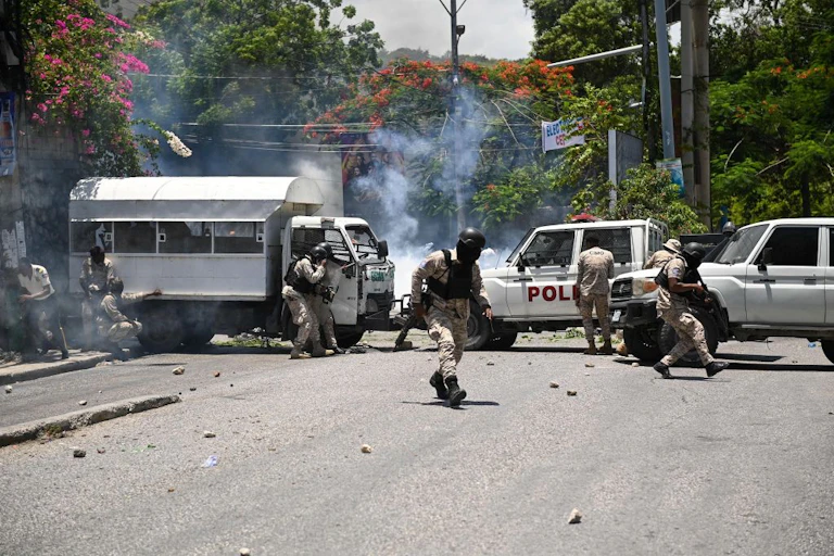 Men in beige-coloured uniform take cover behind a line of white cars that have cut off a road. Smoke billows beyond the cars.