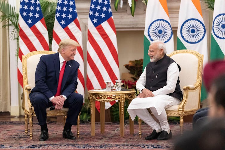 National leaders Trump and Modi sitting on gold-lined chairs in front of US and Indian flags