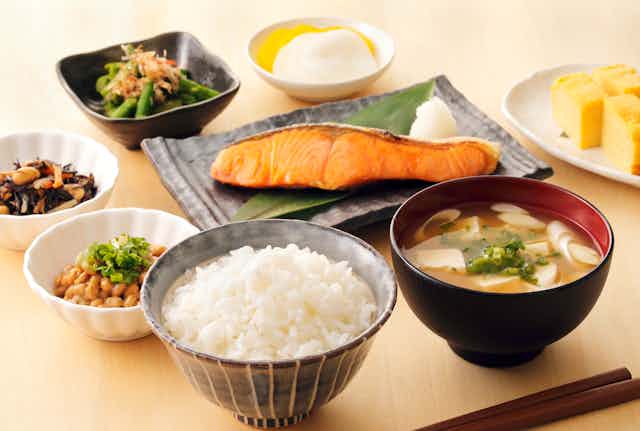 A spread of traditional Japanese foods, including salmon, rice, miso soup, and natto (fermented soybeans).