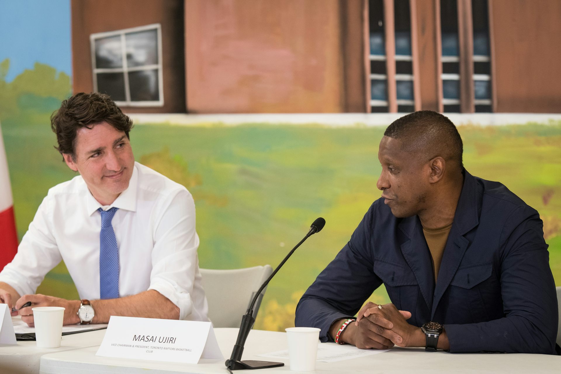 Two men, one in a white shirt and tie and the other in a black shirt, speak at an event.