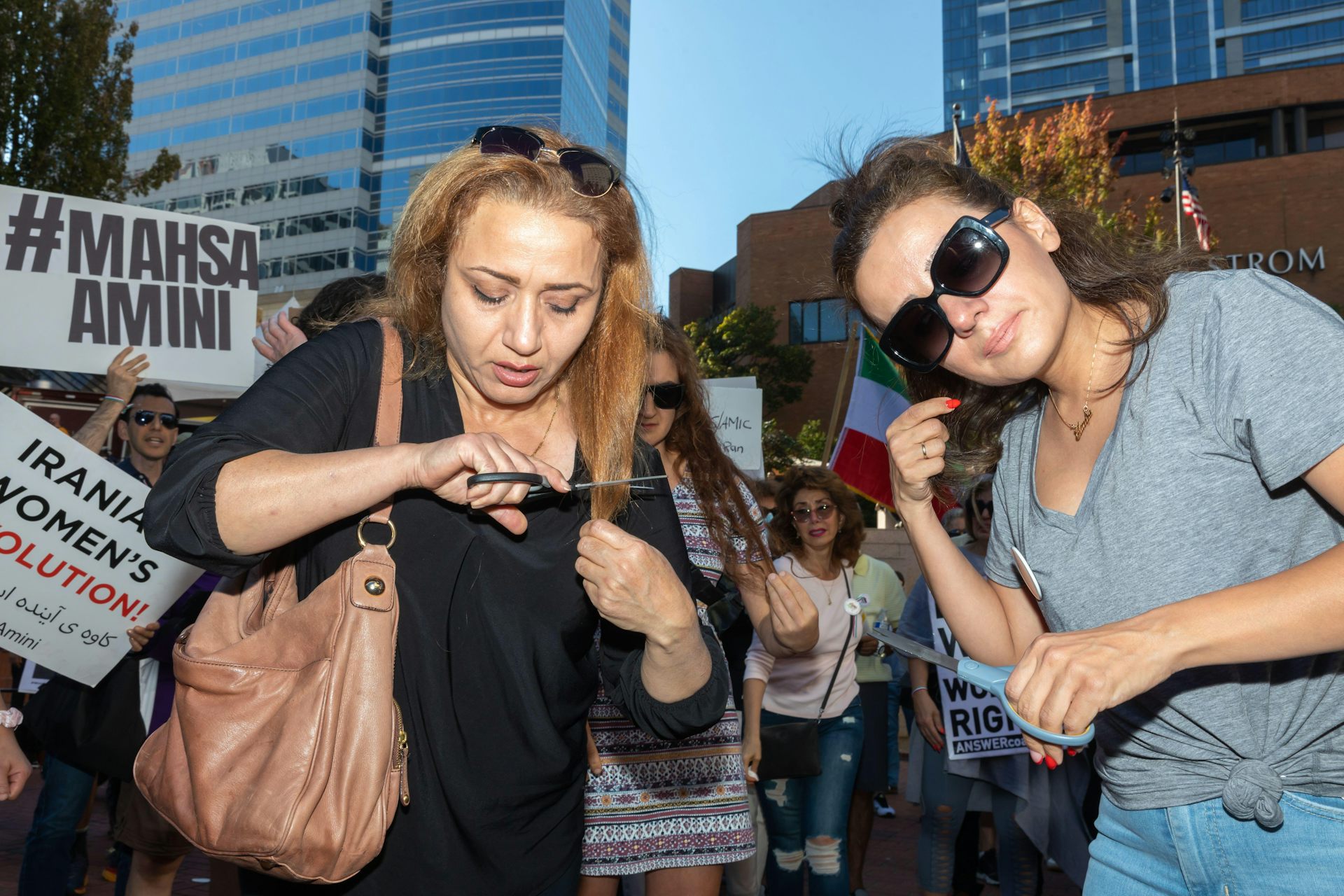 Two women cut their hair surrounded by banners in support of Iranian woman Mahsa Amini, October 2022.