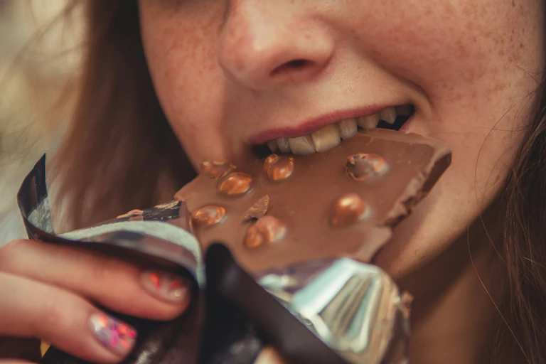 Photo en gros plan d’une femme mordant dans une tablette de chocolat aux noisettes
