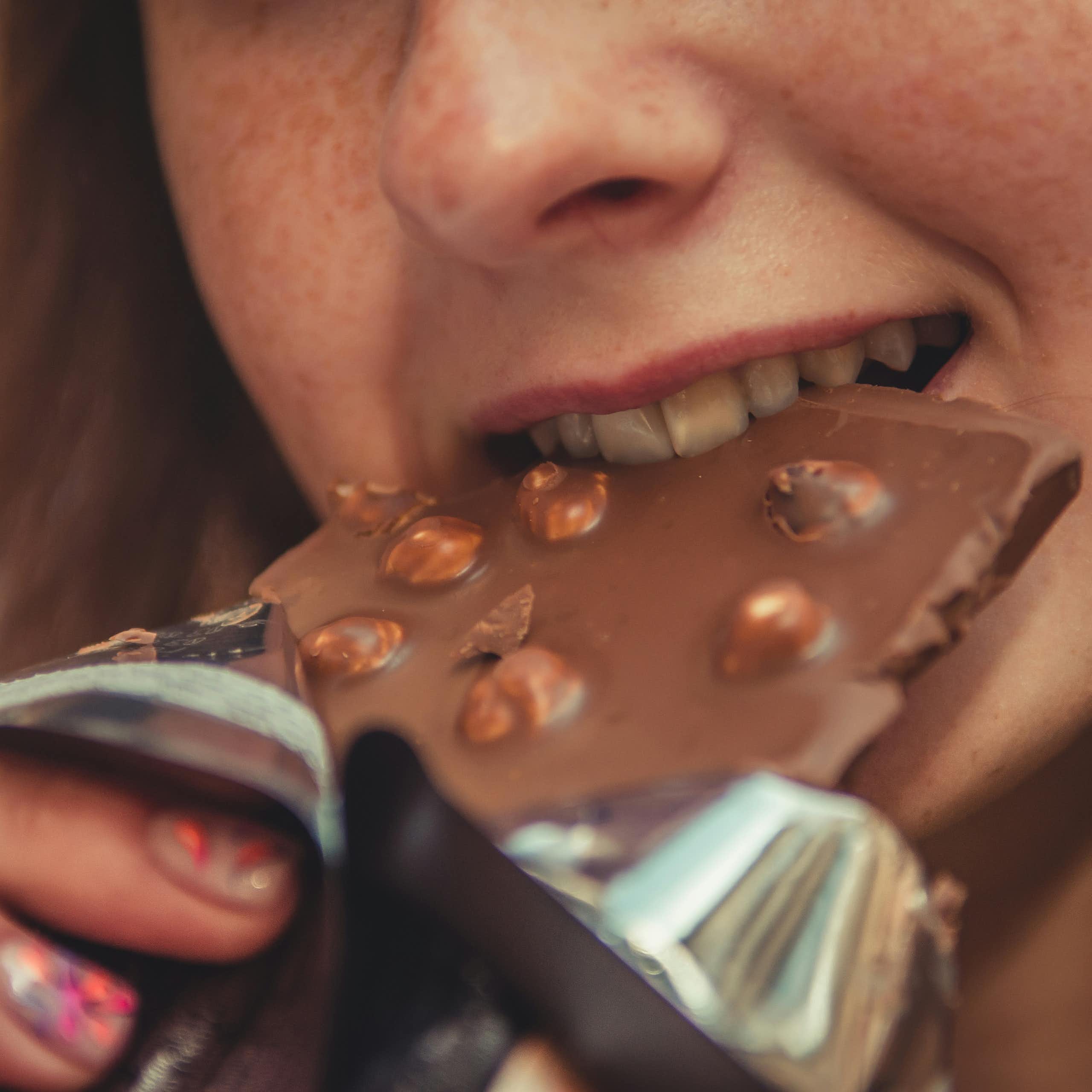 Photo en gros plan d’une femme mordant dans une tablette de chocolat aux noisettes