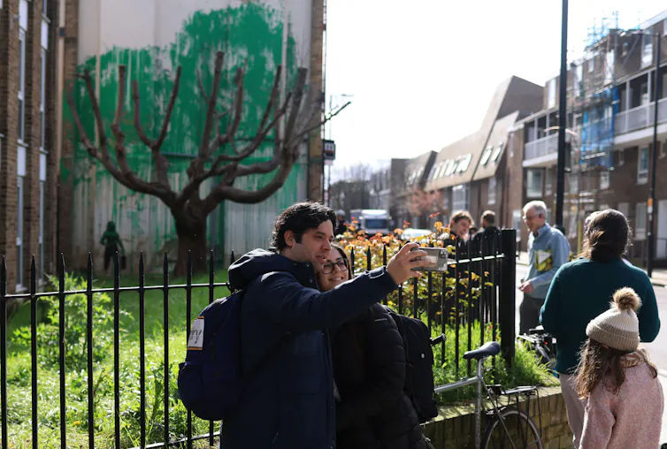 A couple smiling in front of the new Banksy
