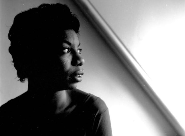 Black and white portrait of young Black woman gazing off into the distance, with her face bathed in light.