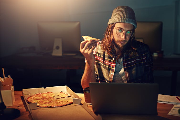 Maneating a pizza in front of a screen.