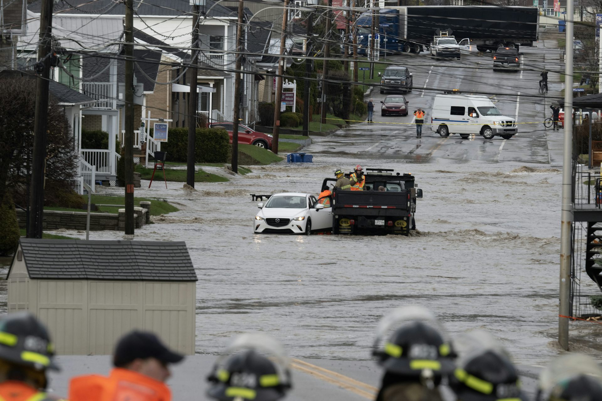 Une rue inondée, où gisent des voitures, avec des secouristes à l’avant-plan