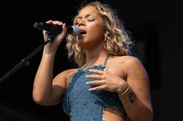 Young Black woman closes her eyes as she sings into a microphone.