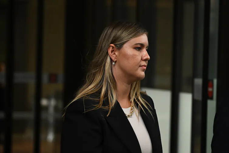The profile of a young woman with long hair in front of a courtroom