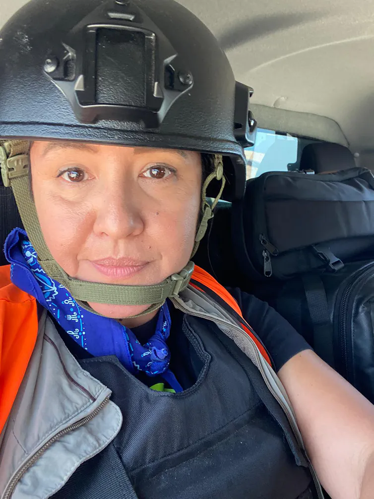 A woman wearing a combat helmet smiles at the camera.