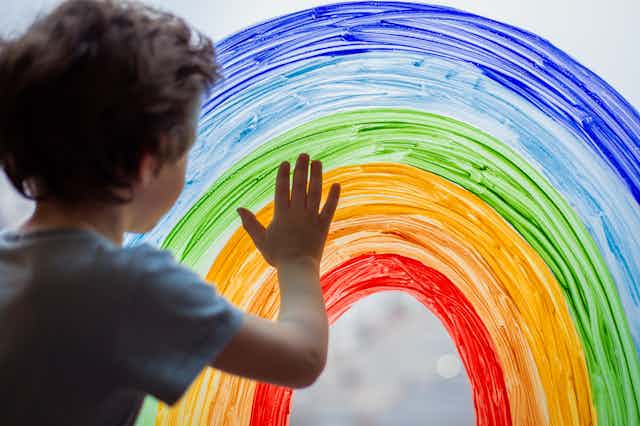 child touches painted rainbow on glass window