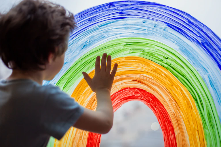 child touches painted rainbow on glass window