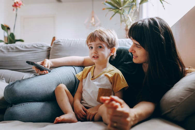 A mother sitting on the couch with her son talking to him.