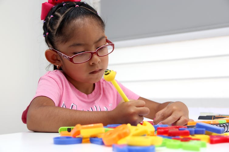 Young girl with glasses is focussed on playing with colourful objects at table