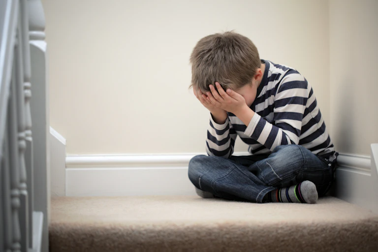 boy sits in corner with face in hands
