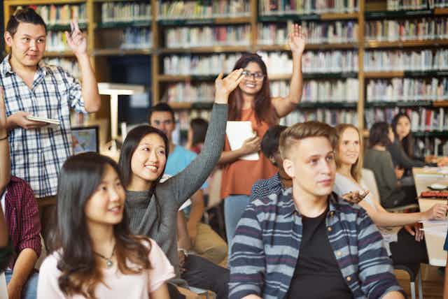 Group of international students raise hands in library tutorial