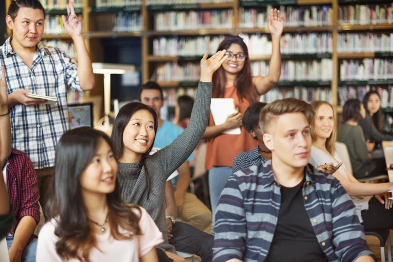 Group of international students raise hands in library tutorial