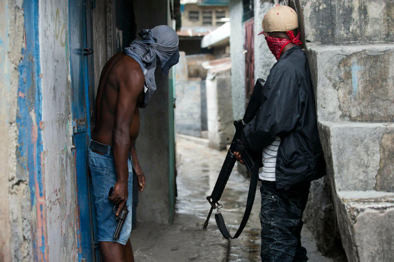 Two men peering down an alleyway holding guns and with their faces covered.