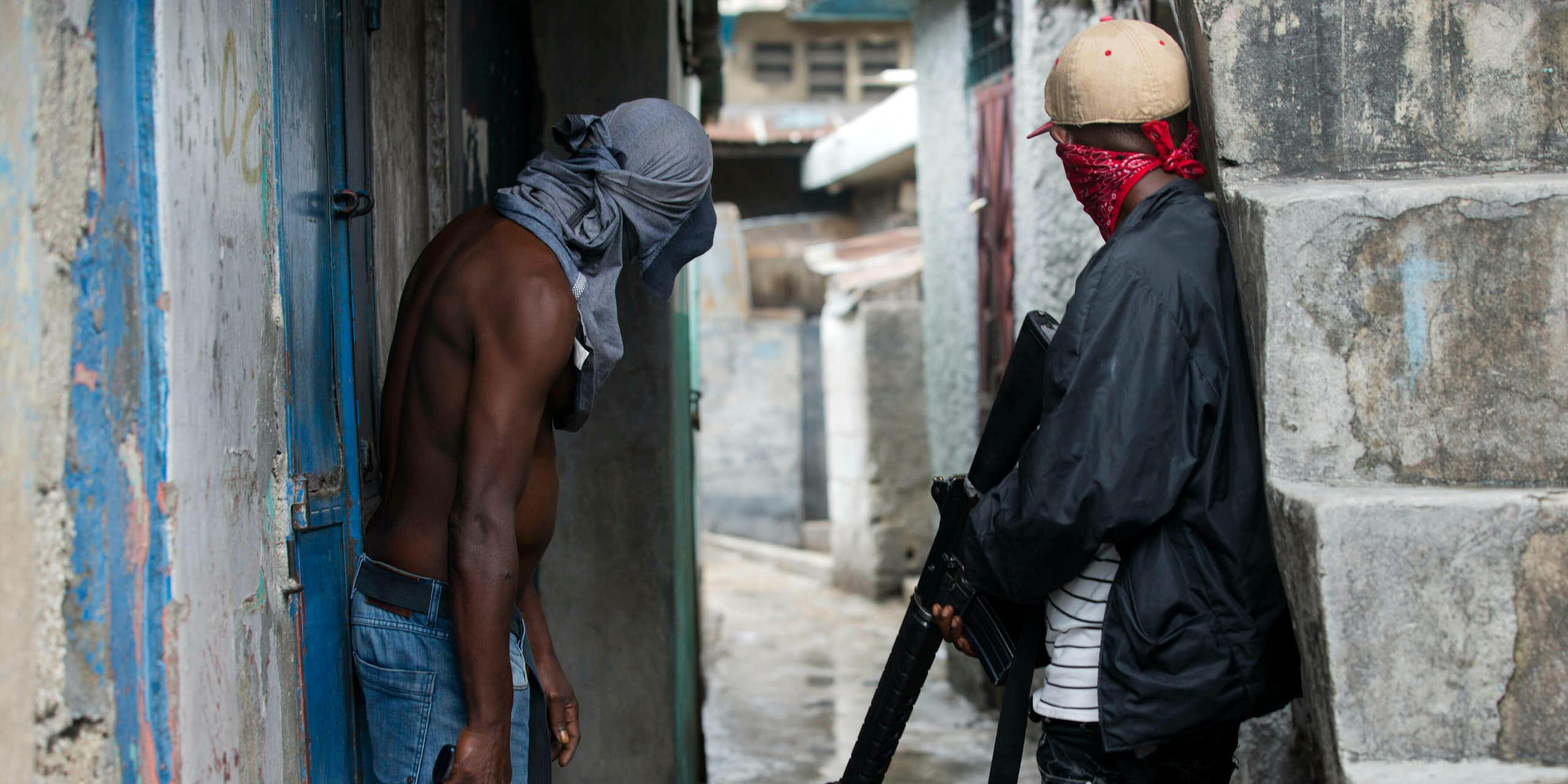 Two men peering down an alleyway holding guns and with their faces covered.