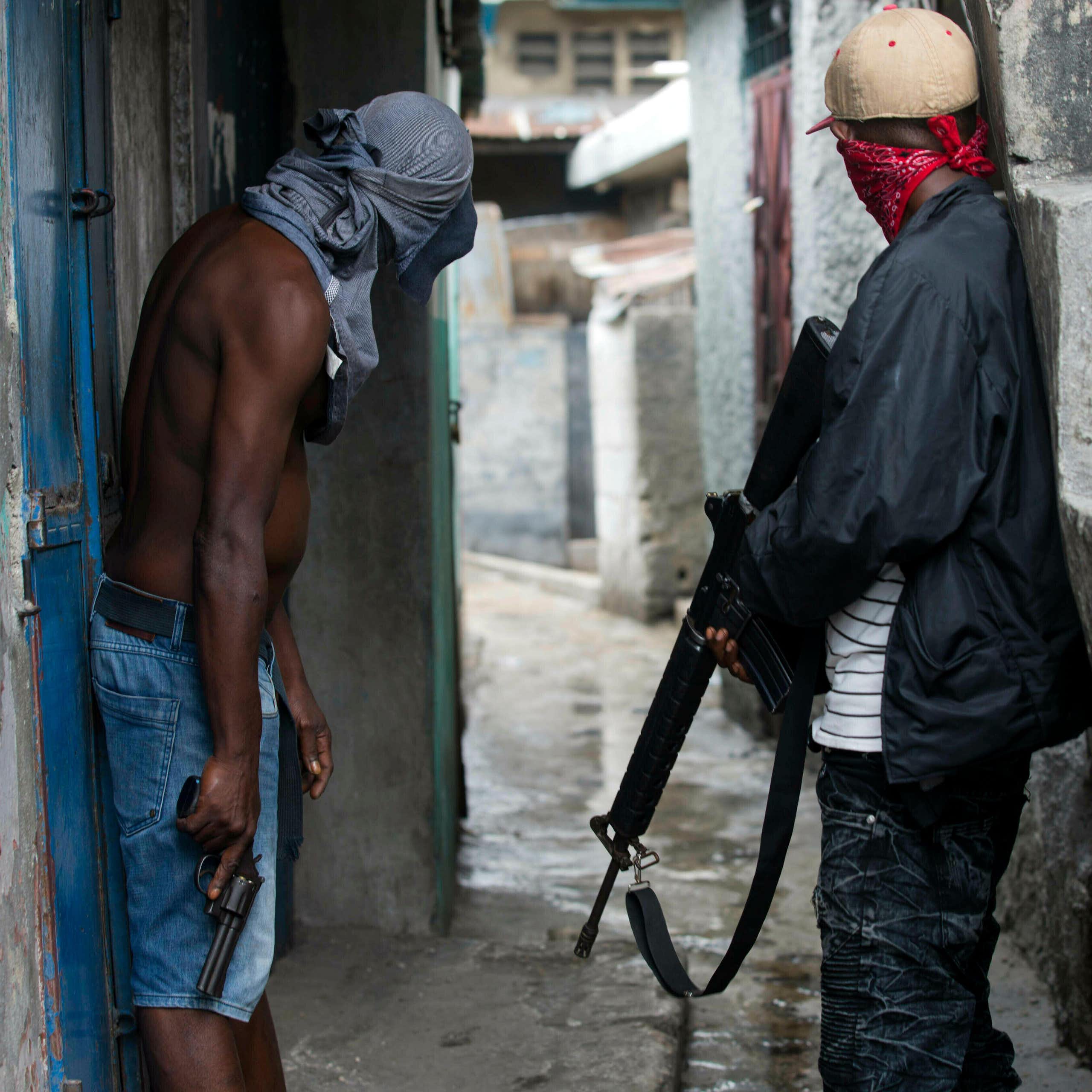 Two men peering down an alleyway holding guns and with their faces covered.