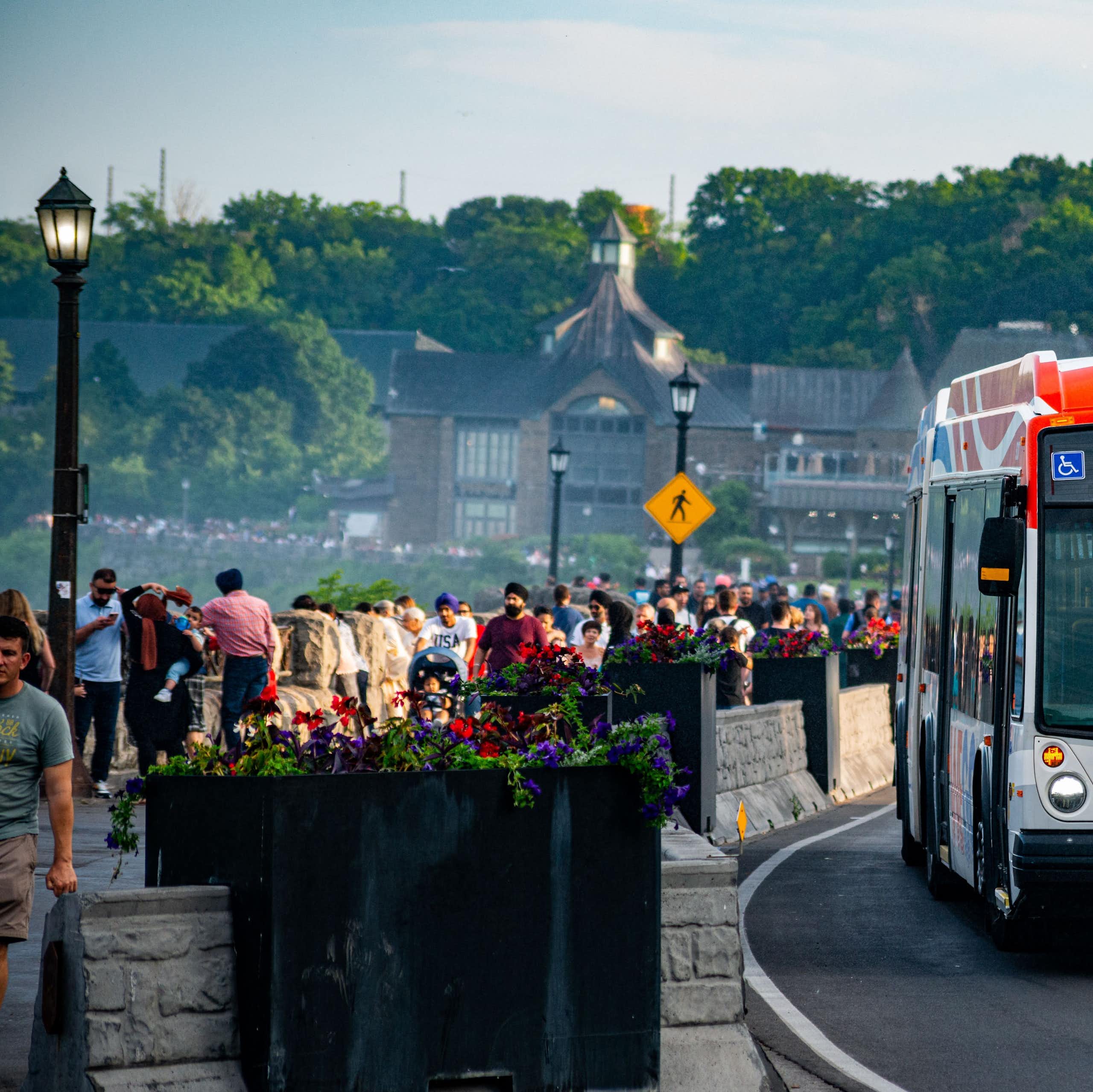 an orange bus drives past throngs of tourists looking at waterfalls