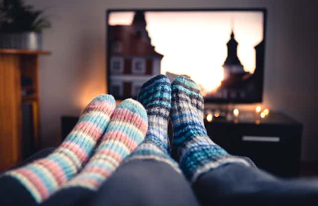 View of a couple's feet in colourful wool socks, up on the coffee table while a television plays in the background