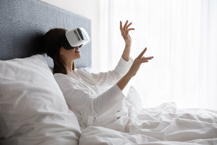 A woman on a bed wears a VR headset