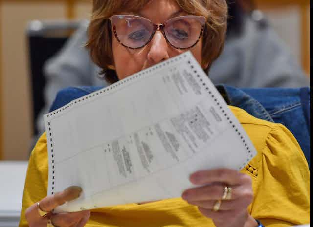 A person wearing glasses holds a printed piece of paper up for a closer look.