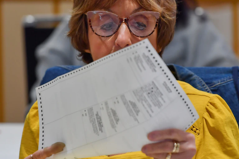 A person wearing glasses holds a printed piece of paper up for a closer look.