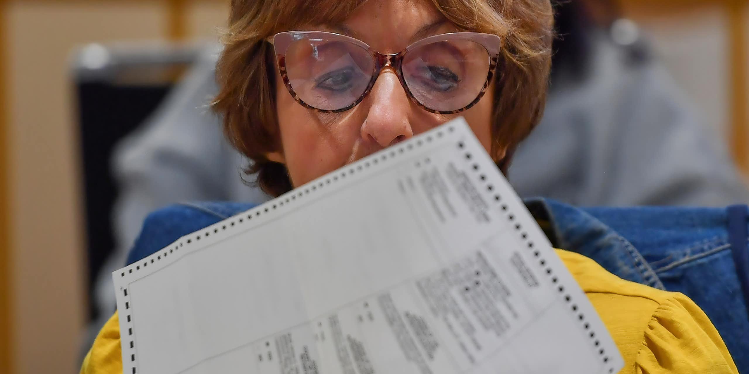 A person wearing glasses holds a printed piece of paper up for a closer look.