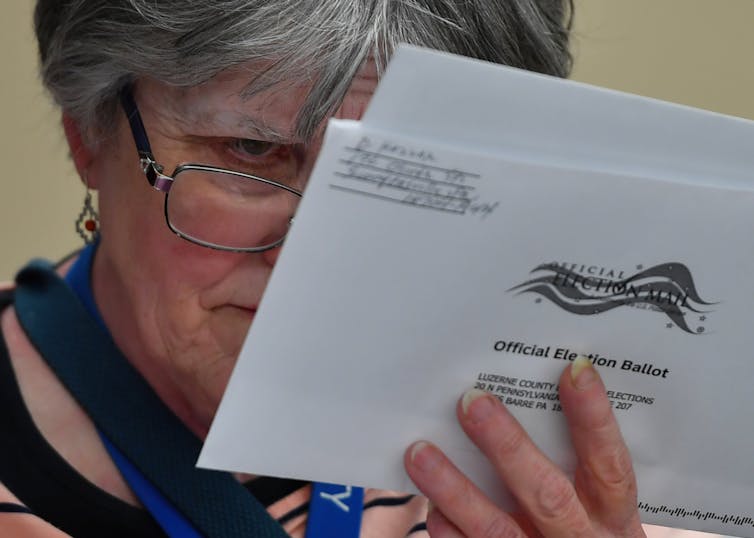 Una persona que sostiene un trozo de correo electoral mira atentamente el reverso del sobre.