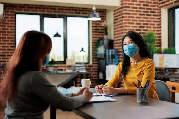 Two women in face masks sitting at a table talking