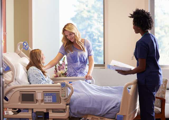 A teen girl in a hospital bed with a parent and a health-care professional