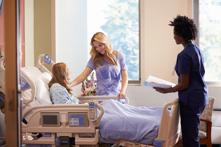 A teen girl in a hospital bed with a parent and a health-care professional