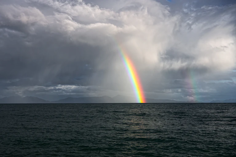 Double rainbows amid stormy clouds over the dark ocean