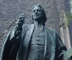 The upper half of a statue of a man with wavy hair in a heavy coat.