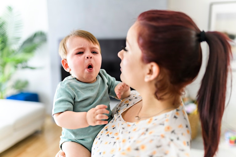 A mother holding a small child who is crying and coughing.