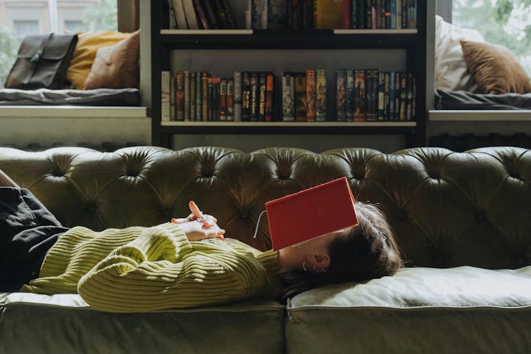 A young woman lies on a couch with an open book over her face.