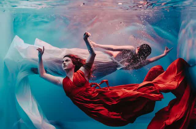 two women in glamorous gowns underwater