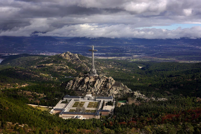 Una cruz gigante en medio de un valle, con un gran edificio a sus pies.