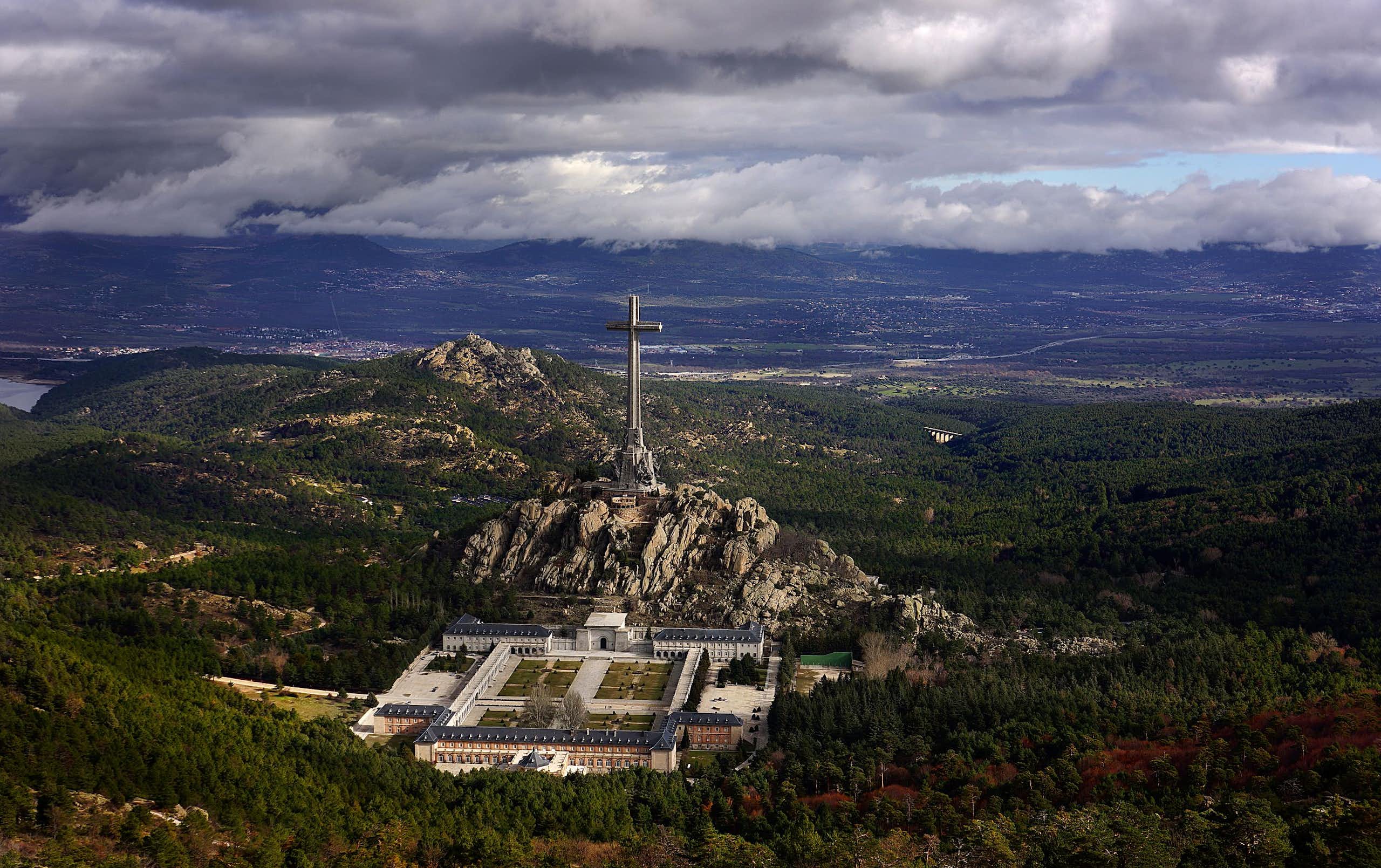 Una cruz gigante en medio de un valle, con un gran edificio a sus pies.