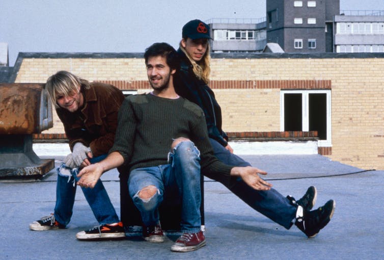 Three members of Nirvana sat on a roof.