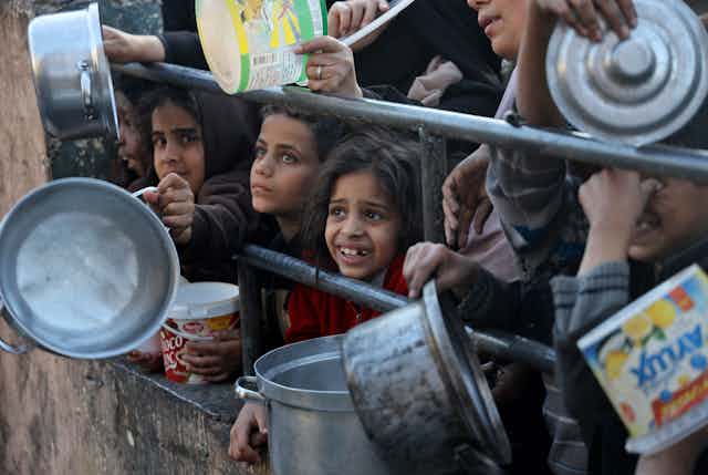 Enfants tendant des gamelles à travers une clôture
