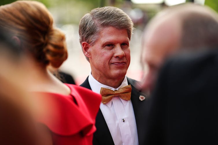Man with graying hair wearing a tuxedo and gold bow tie.