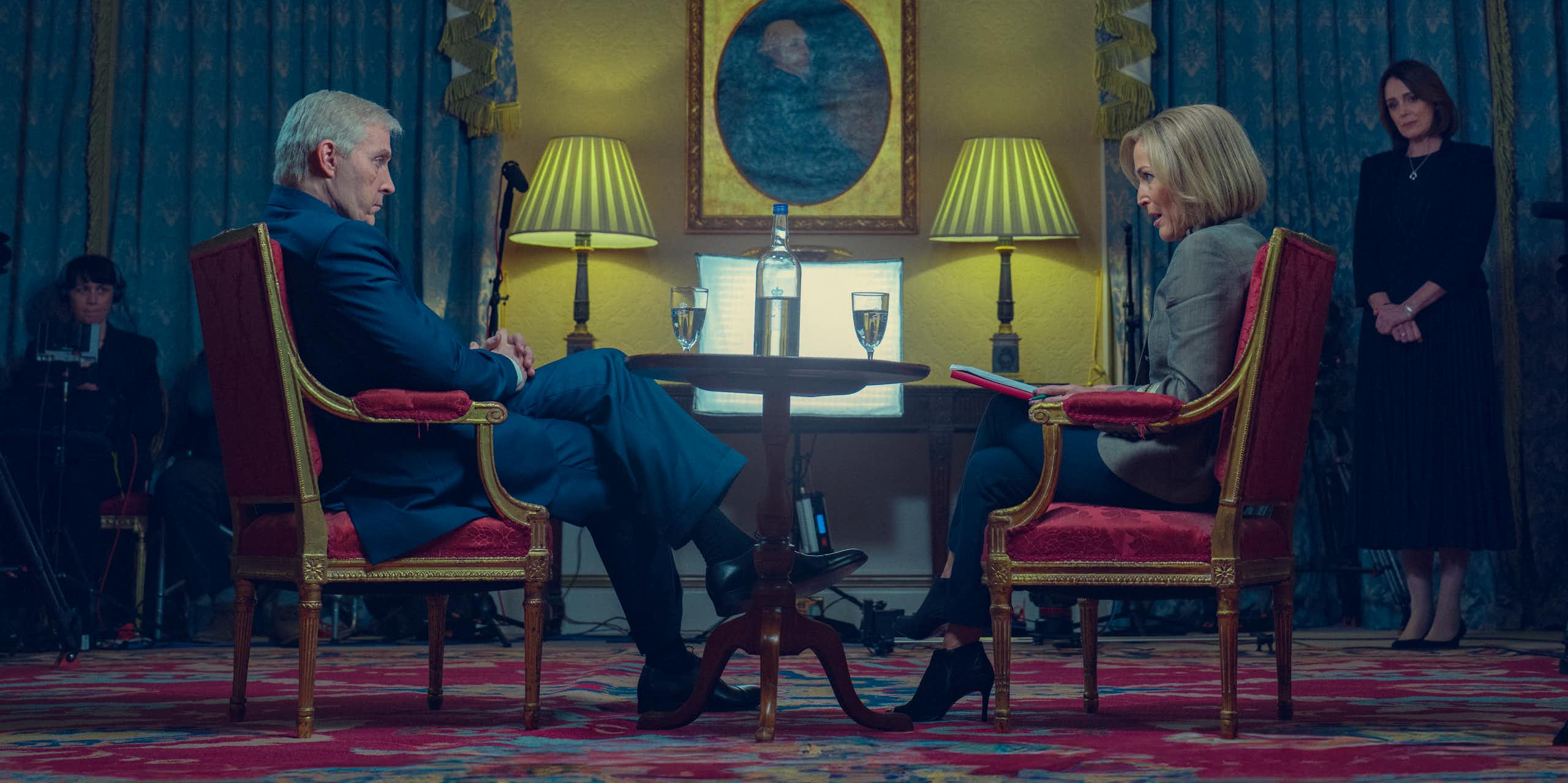 Still image of Sewell and Anderson in character, seated in red chairs doing the infamous Newsnight interview beneath tv cameras and lights