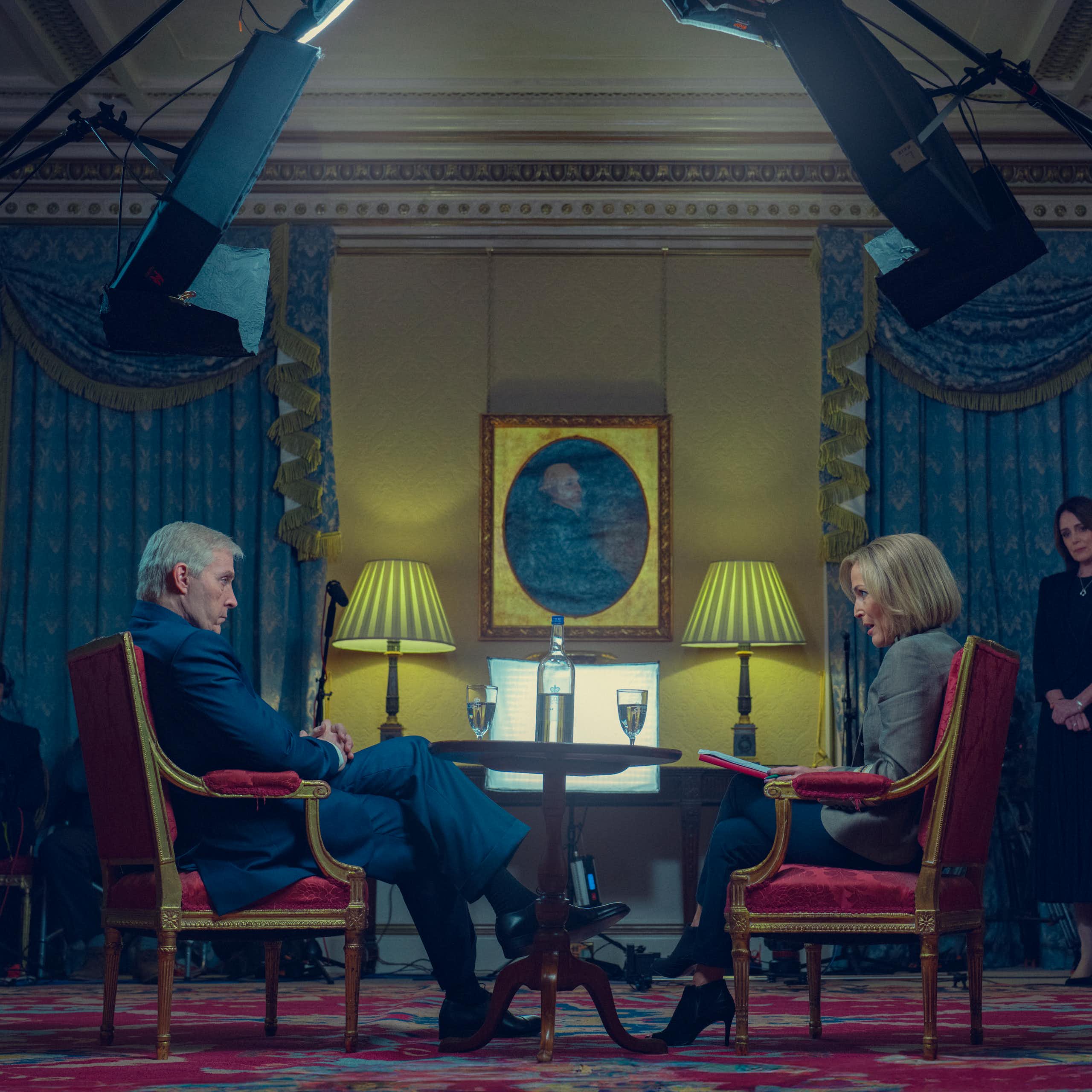 Still image of Sewell and Anderson in character, seated in red chairs doing the infamous Newsnight interview beneath tv cameras and lights