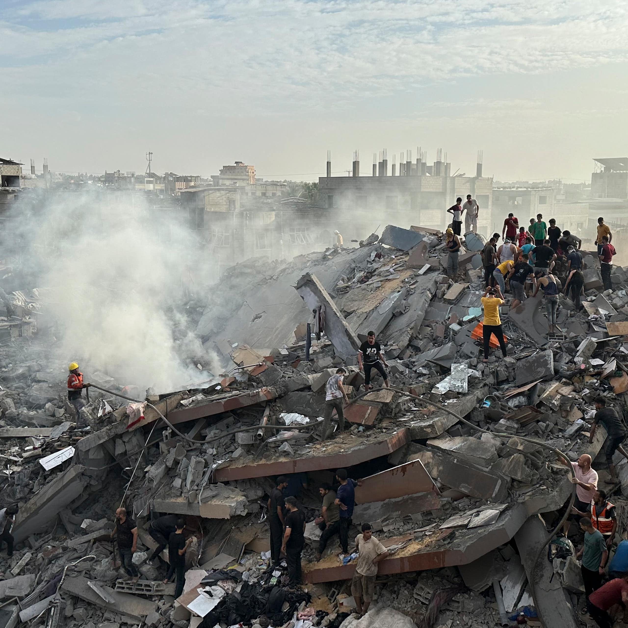 Workers and residents stand on a pile of rubble with one building standing in the background.