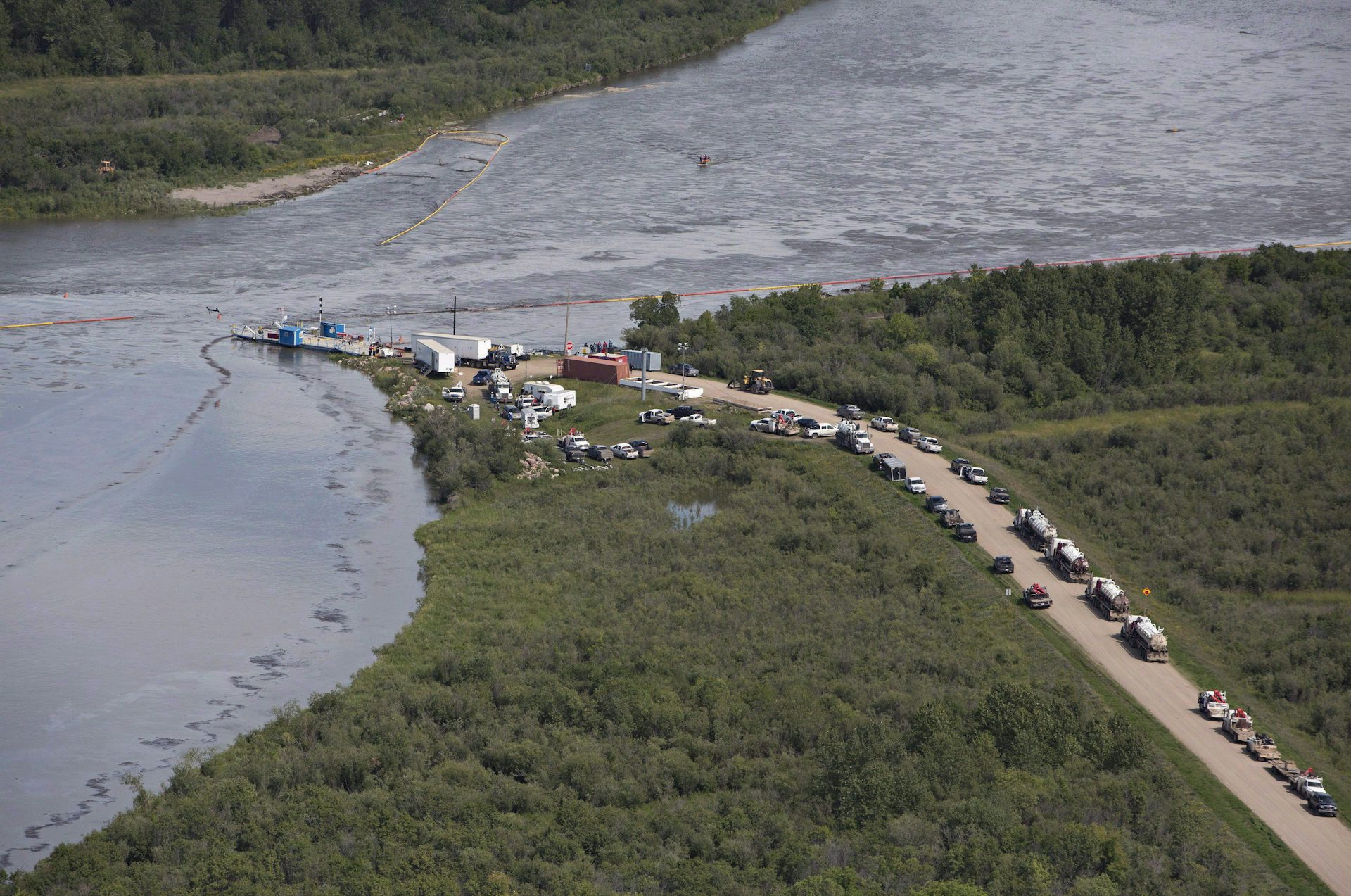 People and vehicles stand near an oily river.